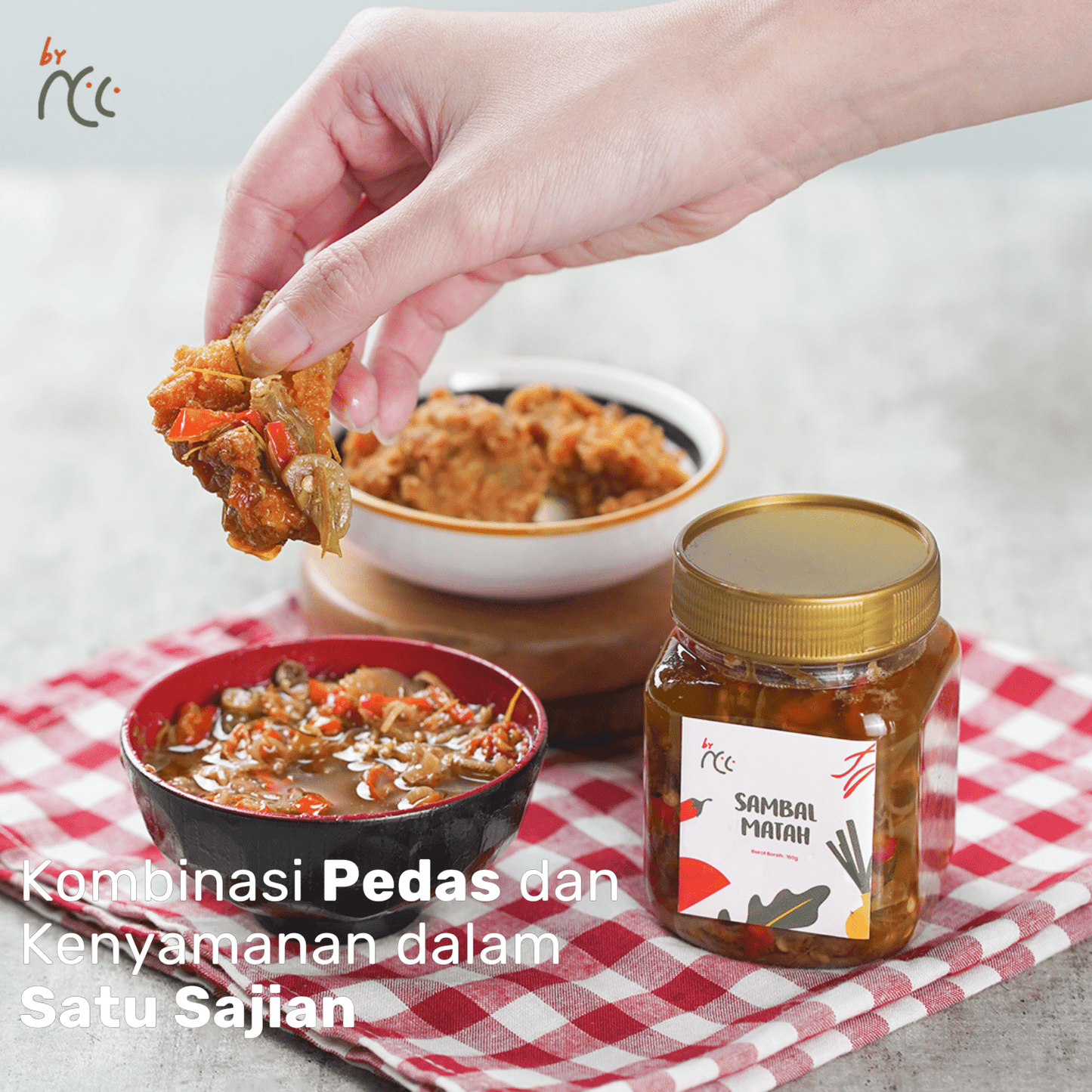 Jar of By NCC Sambal Matah with spicy Indonesian chili sauce and hand dipping food on checkered cloth